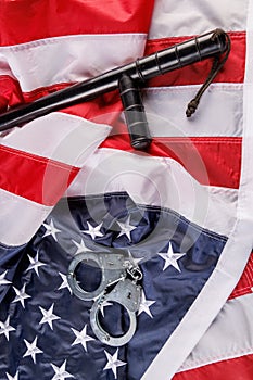 silver metal handcuffs and police nightstick over US flag on flat surface