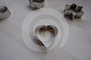 Silver metal heart-shaped biscuit cutter, mold for baking on white background across other shaped-biscuit molds. Copy space