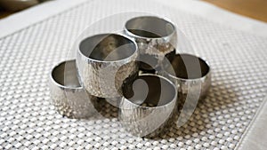 Silver metal napkin rings holders over a golden color place mat. Ready for table setting in an event, party or holiday