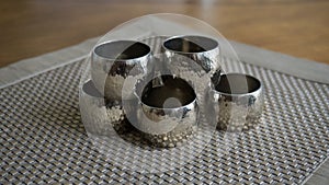 Silver metal napkin rings holders over a golden color place mat. Ready for table setting in an event, party or holiday