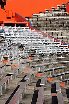 Silver metal stadium seats in sun surrounded by benches and orange