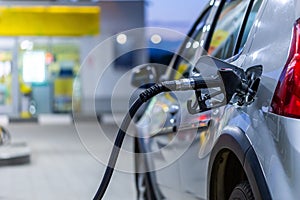 Silver metallic color car refueling on night gas station - close-up with selective focus and blurry bokeh background