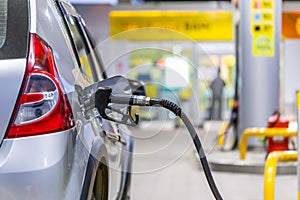 Silver metallic color car refueling on night gas station - close-up with selective focus and blurry man silhouette in