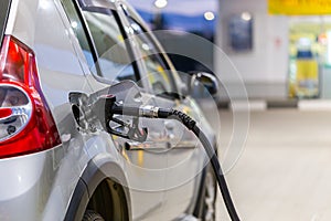 Silver mettalic color car refueling on night gas station - close-up with selective focus and blurry background