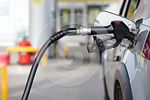 Silver mettalic color car refueling on night gas station - close-up with selective focus and blurry background