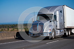 Silver modern big rig semi truck with trailer running on freeway