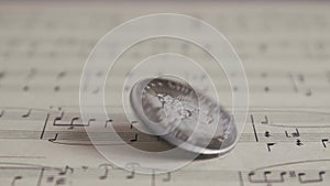 Silver Old Coin Rotating On The Sheet Of Music Close Up. Spinning American Dollars Coin. Payment For Creative Work
