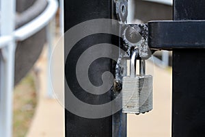 Silver padlock on black wrought-iron metal gate with blurred background