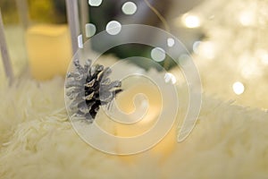 Silver painted pine cone on Merry Christmas and Happy New Year background. Candle standing on white fur carpet.