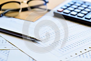 Silver pen on a pile papers with calculator and eyeglasses is background.