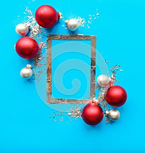 Silver photo frame and red Christmas baubles on bright blue background.