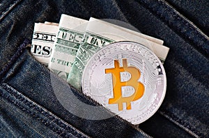 A silver physical Bitcoin coin with golden symbol B and folded American dollars.