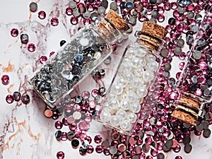 Silver and pink rhinestones and white pearls in glass jars with wooden lids on a marble background