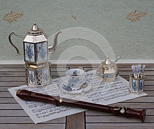 English tea set, silver-plated teapot, spoon vase and teaspoon, sugar bowl and sugar spoon and a block flute on a sheet of music