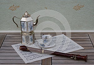 English teacup and saucer, silver-plated teapot on a silver stove, with floral decor and a block flute on a sheet of music