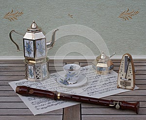 Teacup, silver-plated teapot on a silver stove sugar bowl and sugar spoonmetronome for music and a block flute on a sheet of music