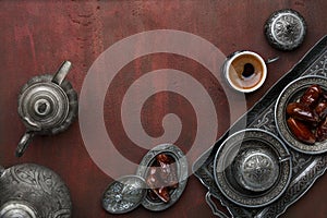 Silver plates with date fruits, Arabic coffee pot and cups on the dark red-brown wooden background. Ramadan background. Ramadan Ka