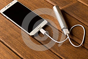 Silver power bank charging smartphone on wooden table