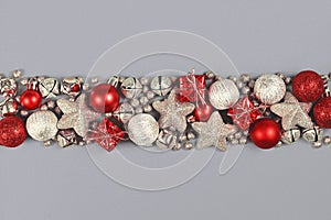 Silver and red Christmas ornaments like small gift boxes, round baubles, bells and stars forming line on gray background