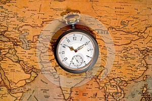 Silver retro pocket watch lying on a paper old world map. Antique gray round clock with a dial and golden hands on a