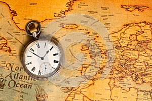 Silver retro pocket watch lying on a paper old world map. Antique round clock with a dial and arrows on a geographical