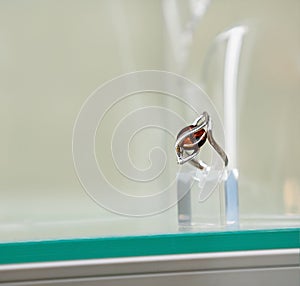 Silver ring with amber eye on a glass shelf