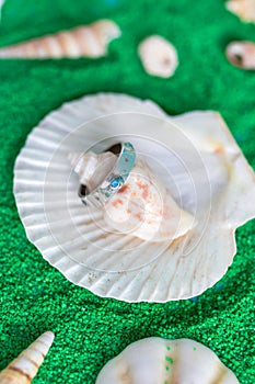 Silver ring with blue stones on a background with artificial green sand and seashells. Handcraft jewelry.