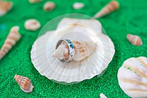 Silver ring with blue stones on a background with artificial green sand and seashells. Handcraft jewelry.