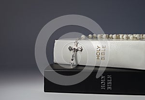 Silver rosary with white beads hanging over 2 closed bibles
