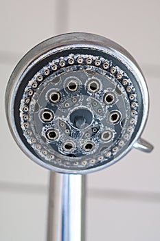 Silver round shower head with hard water deposit all around the sprinklers close up macro side shot  against light gray