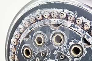 Silver round shower head with hard water deposit all around the sprinklers close up macro side shot  against white