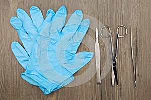 Silver scalpel surgical scissors and forceps beside blue latex glove