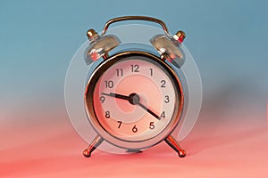 Silver shiny alarm clock in retro vintage style on blue red neon background. Minimal modern style