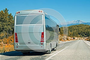 Silver shiny gray modern comfortable tourist bus driving through highway at bright sunny day mountains. Travel and coach tourism