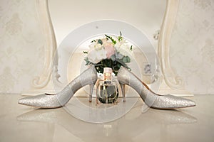 Silver shoes of the bride , perfume, bouquet and wedding rings on the dressing table near the mirror.