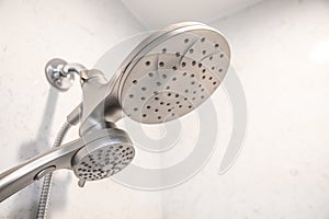 A silver shower head in a white modern shower