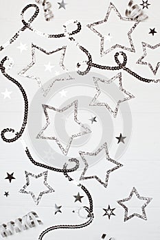 Silver sparkling stars with sequin chain on white wooden background.