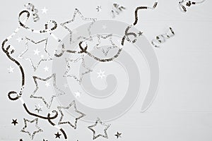 Silver sparkling stars on white wooden background.