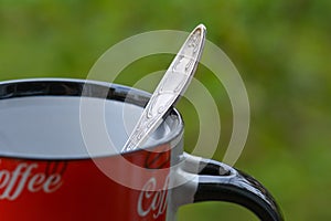 Silver spoon in red coffee mug on green background