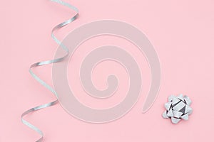 Silver streamers serpentine and bow on pink background in minimal style. Concept decorations for celebration, party, holiday,