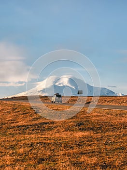 A silver SUV is driving along the highway route to the dawn snow-covered Elbrus. Autumn beautiful road through the mountain desert