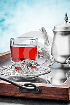 Silver teapot with a cup fruit tea in a cup holder on a mirror tray