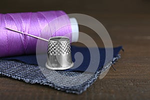 Silver thimble, thread and needle on wooden table, space for text. Sewing accessories