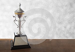 Silver trophy on wooden table on bokeh background. Winning awards with copy space.