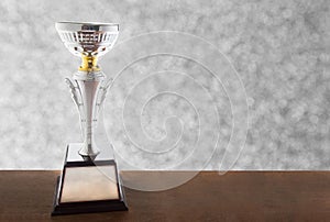 Silver trophy on wooden table on bokeh background. Winning awards with copy space