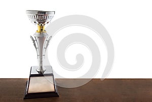 Silver trophy on wooden table isolated over white background. Winning awards with copy space.