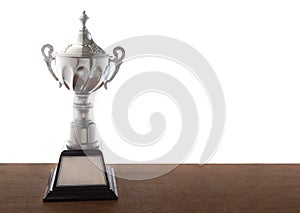 Silver trophy on wooden table isolated over white background. Winning awards with copy space.