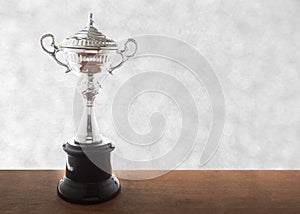 Silver trophy on wooden table over abstact white bokeh background. Winning awards with copy space.