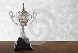 Silver trophy on wooden table over white background. Winning awards with copy space.