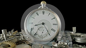 Silver vintage pocket watch dial on pile of clockwork parts. Round old clock among metal gears and cogwheels